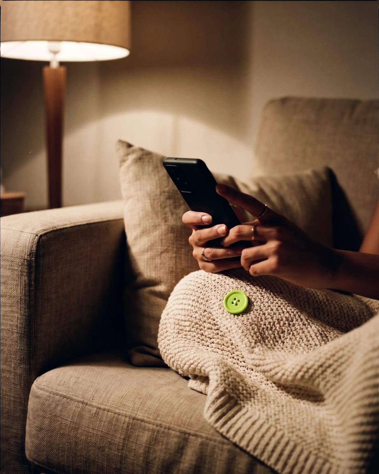 Mãos segurando o celular no sofá de casa à noite